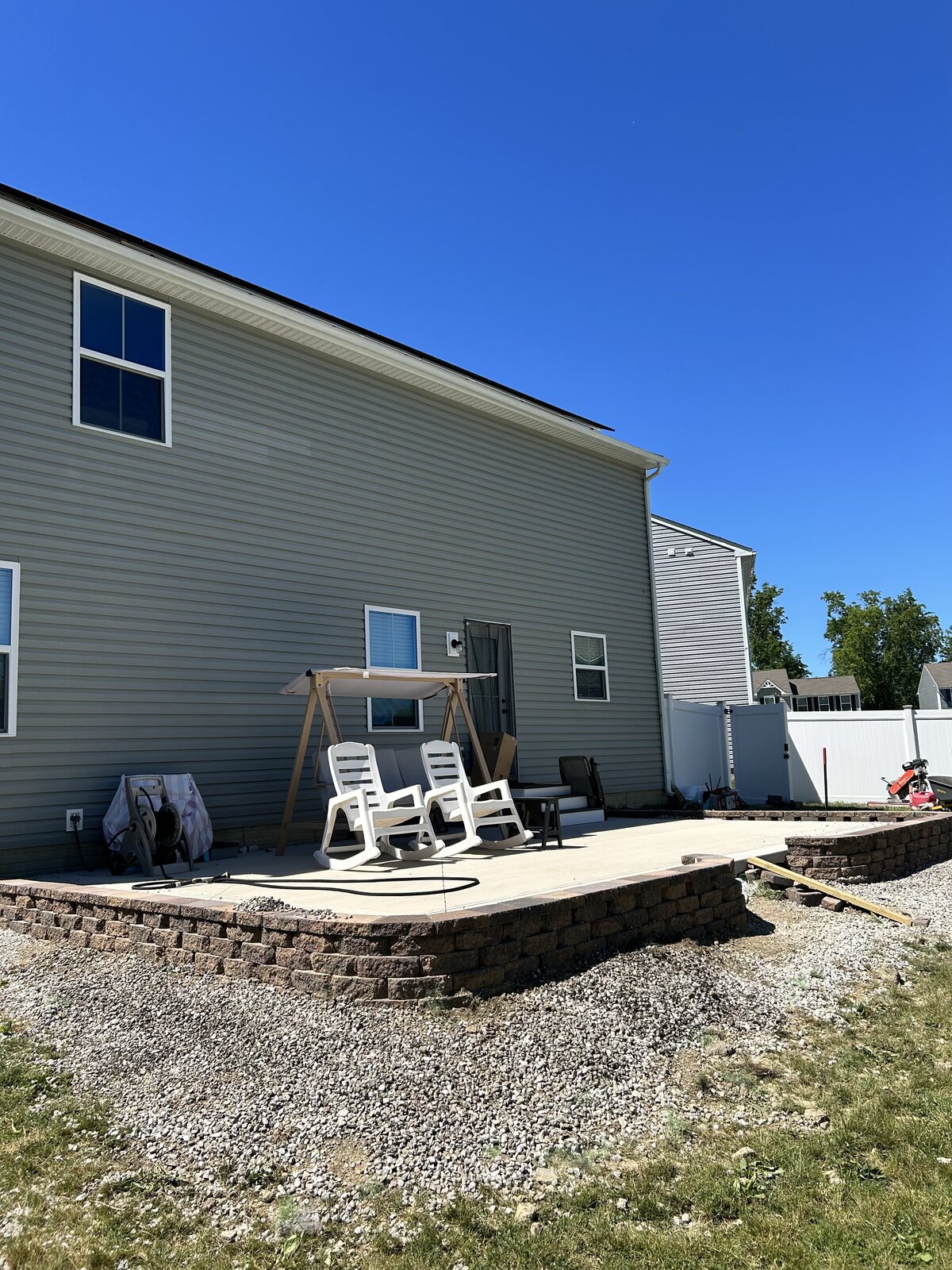 Raised paver patio with stone retaining wall built against the side of a home