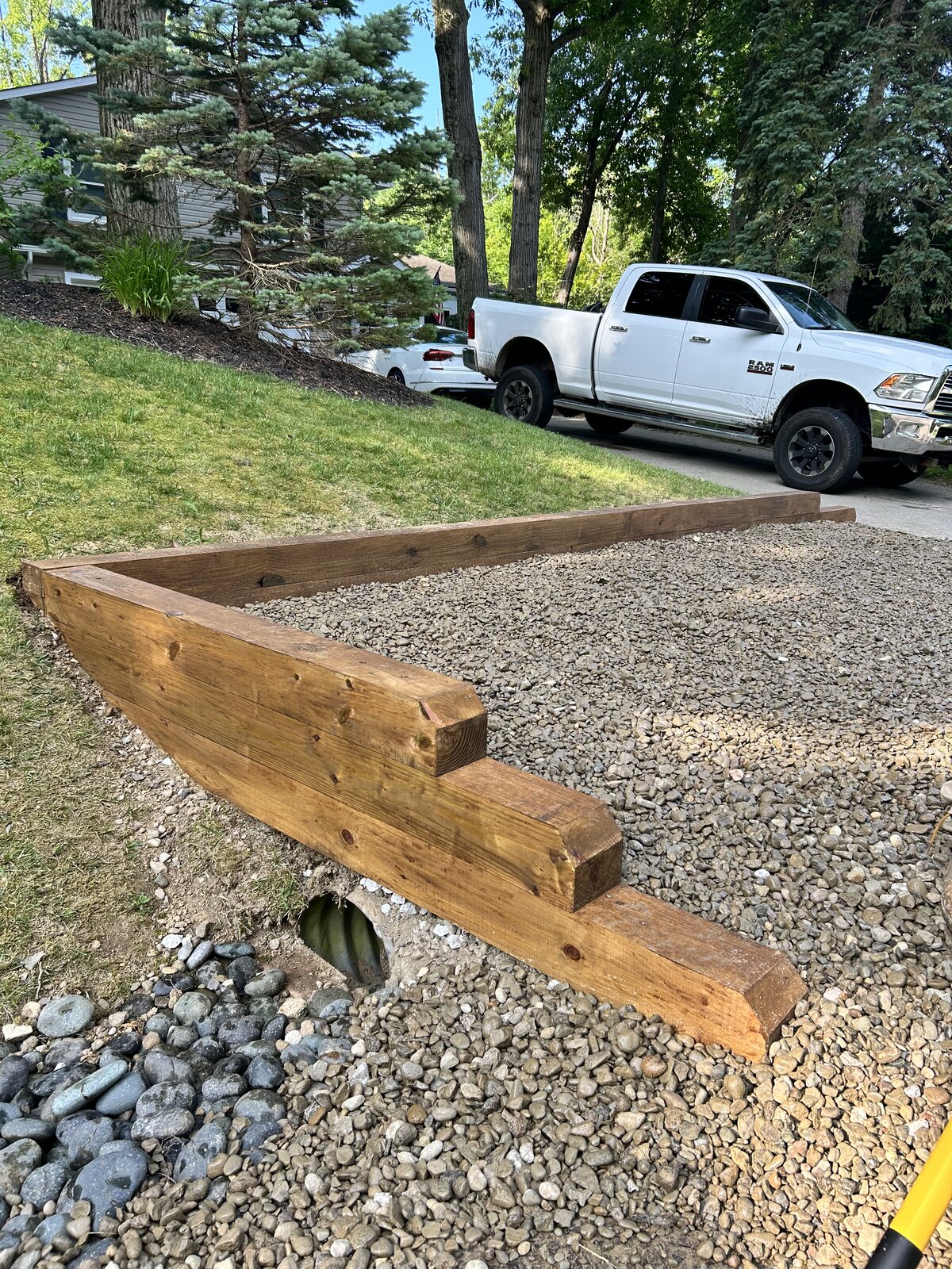 Custom timber-framed gravel driveway edge with river rock drainage border